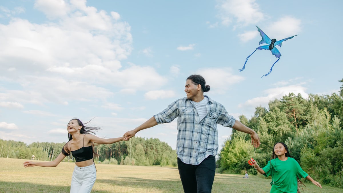 A joyful family running in a park, flying a dragon kite under a blue sky.